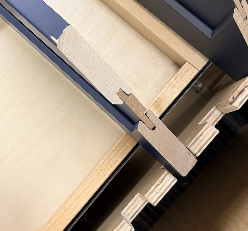Close view of a cut cabinet sample showing exposed material behind a painted surface, a narrow insert seated in a joint and a layered box edge.